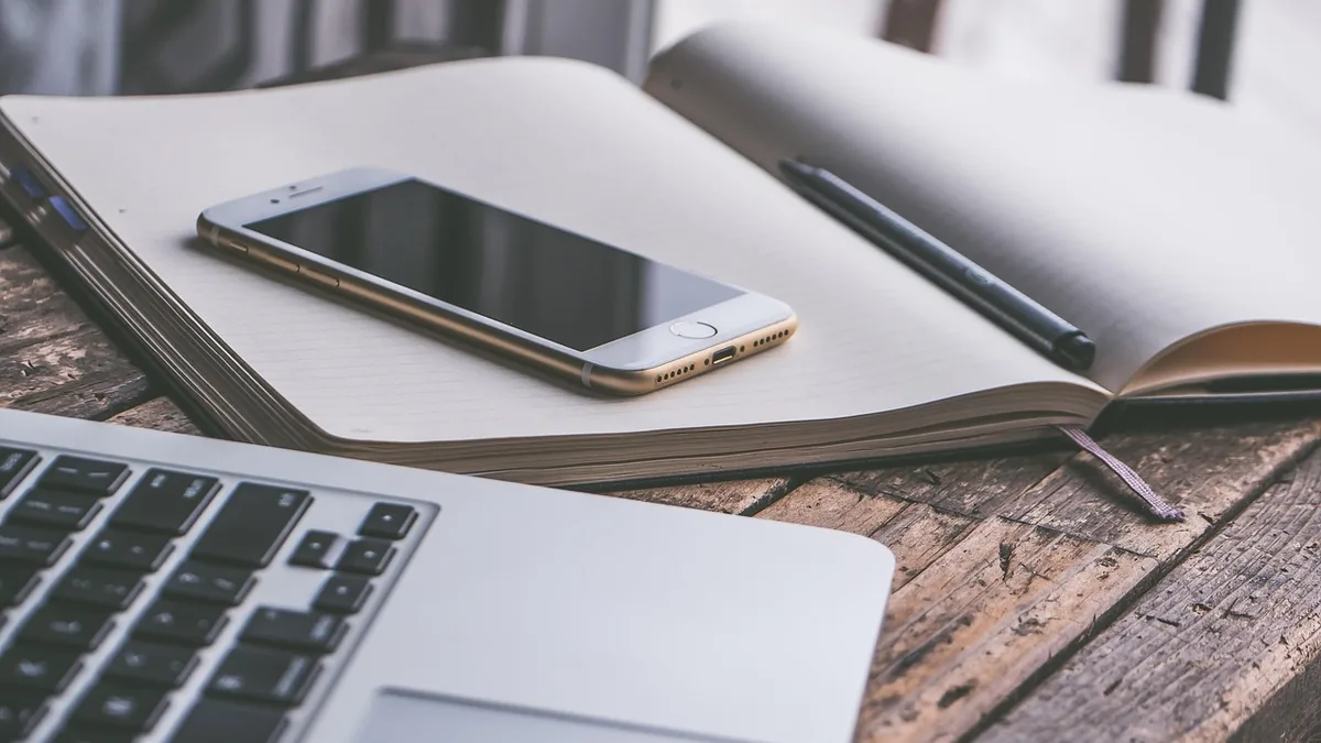 A mobile phone and laptop on a wooden desk