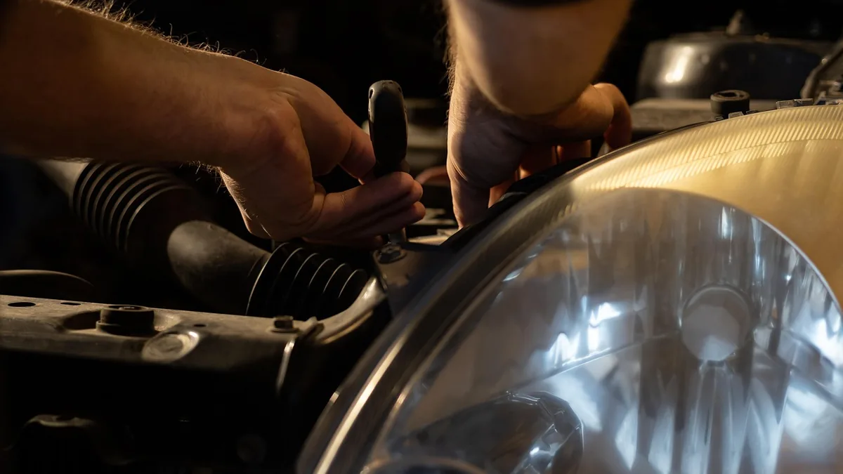 A mechanic&rsquo;s hands at work behind a car headlight