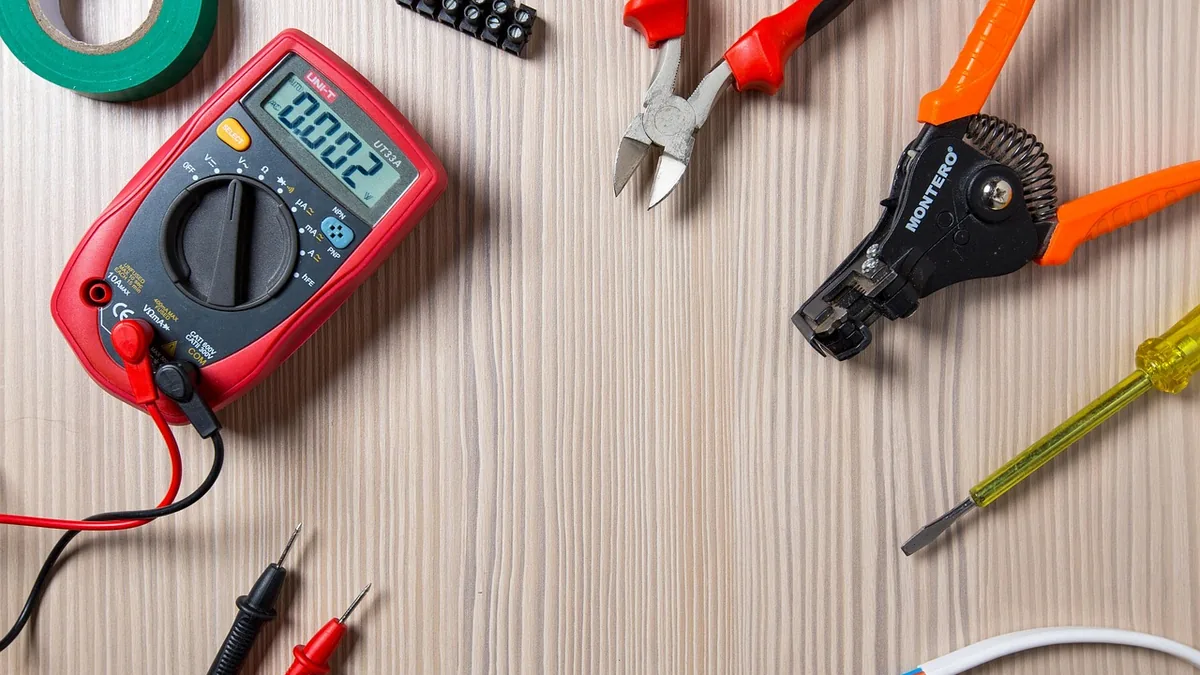 A multimeter, side cutters, wire strippers, a screwdriver and cable laid out on a workbench